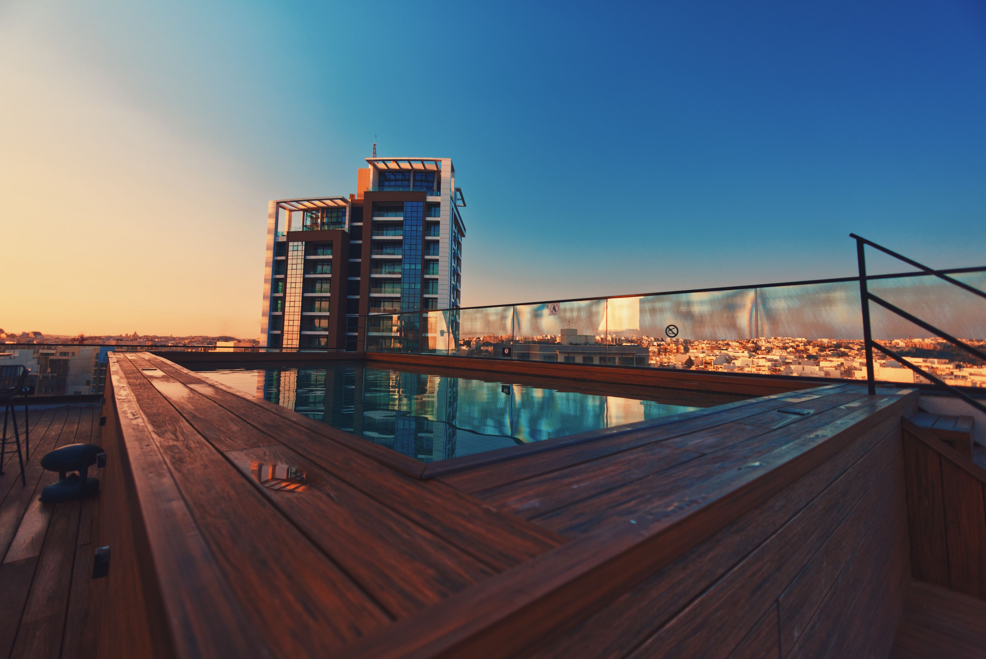 Una piscina en la azotea con un deck de madera y vistas a un paisaje urbano.