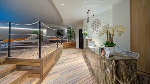 Una moderna área de recepción con suelo de madera, mostrador de recepción, zona de estar con una hamaca y un letrero en la pared que dice