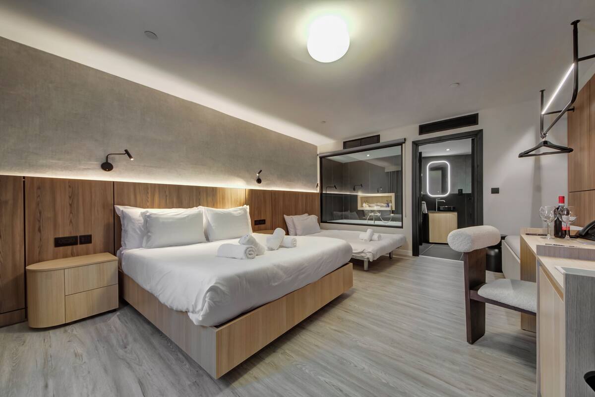 A modern hotel room with a large bed, bedside tables, a desk, and a mirror.