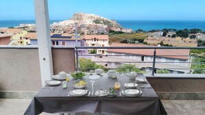 Een eettafel op een balkon met uitzicht op een kustplaatsje en een fort op een heuvel.