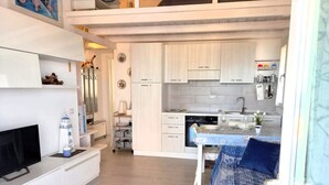 Een knus woongedeelte met een kitchenette, een eethoek en een zithoek met een blauwe sofa met een patroon.