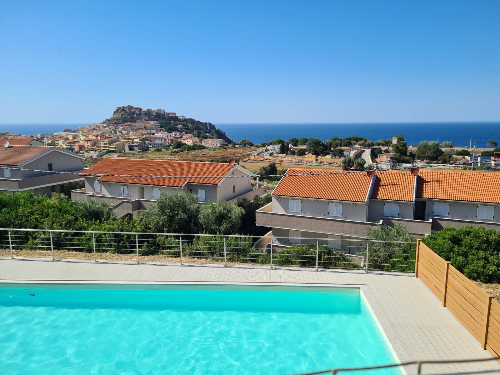 A swimming pool with a view of a coastal town and a hill with a castle-like structure in the background.
