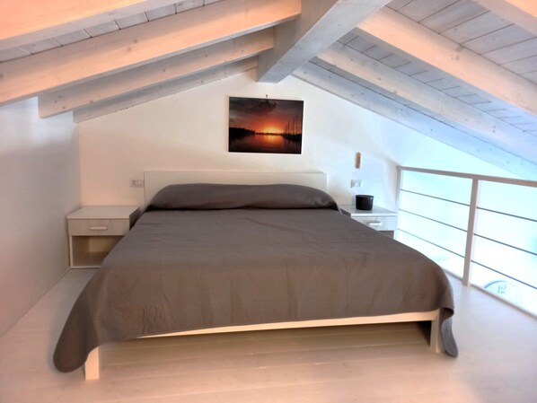 A bedroom with a bed, nightstands, a wall-mounted painting, and a window. - Affittimoderni Castelsardo - Luxury Penthouse (Castelsardo)