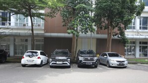 Vier Autos sind vor einem Gebäude mit großen Fenstern und Bäumen in einer Reihe geparkt.