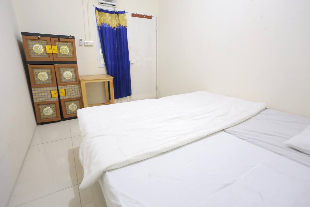 Ein Schlafzimmer mit Bett, Kleiderschrank, einem kleinen Tisch und einem Vorhang.