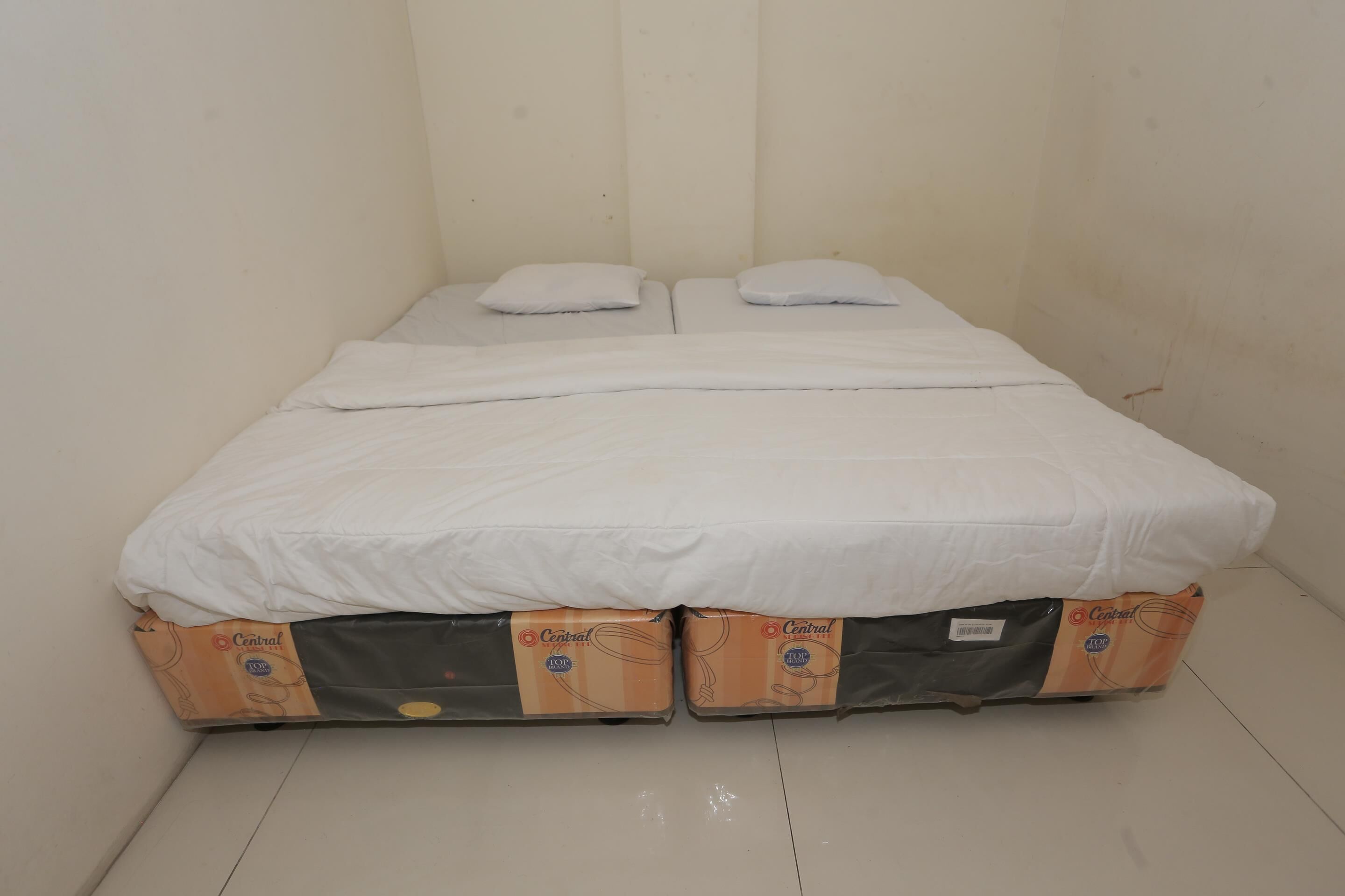 A bed with white bedding and two pillows, placed in a room with plain walls and a tiled floor.