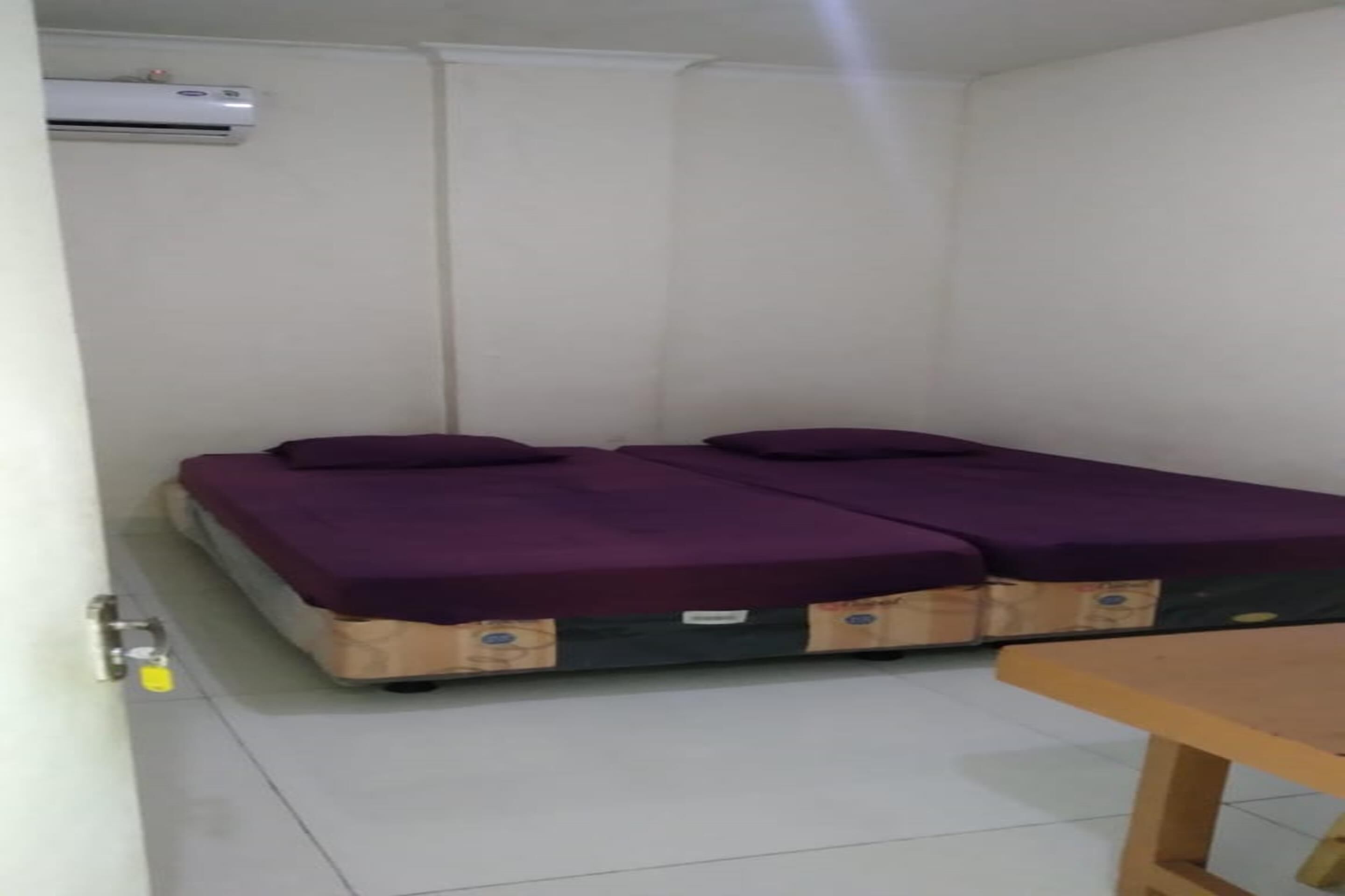 A room with two beds, a wooden table, and an air conditioning unit.