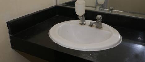 Un lavamanos blanco con grifo y dispensador de jabón sobre una encimera negra.