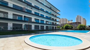 A modern building with a pool area, featuring a large circular pool and a rectangular pool, surrounded by a tiled deck.