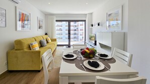 A modern apartment with a yellow sofa, dining table set for four, and a balcony with a city view.