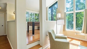 Une pièce spacieuse avec un plancher en bois, un canapé, une lampe et une grande fenêtre donnant sur les arbres.