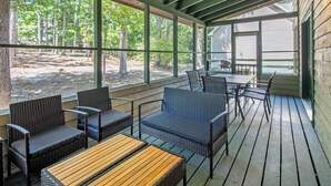 Un espace extérieur aménagé, abrité et doté de meubles en osier et d’une table en bois, offrant une vue sur une zone boisée.