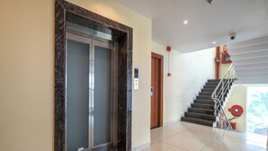 A modern elevator with a marble frame, a staircase with metal railings, and a fire alarm on the wall. - Hotel Radhe Krishna Resort (Ujjain)