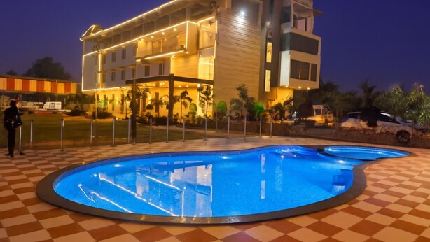 A hotel with a pool area, a checkered floor, and a building with multiple balconies. - Hotel Radhe Krishna Resort (Ujjain)