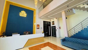 A modern hotel lobby with a reception desk, a blue sofa, a staircase, and a chandelier. - Hotel Radhe Krishna Resort (Ujjain)