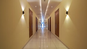 A long, well-lit hallway with wooden doors and wall-mounted lighting fixtures. - Hotel Radhe Krishna Resort (Ujjain)