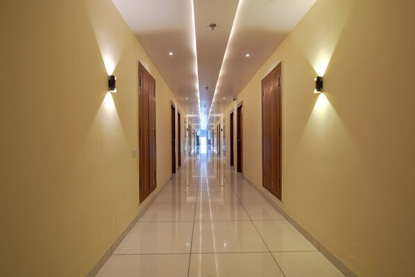A long, well-lit hallway with wooden doors and wall-mounted lighting fixtures.