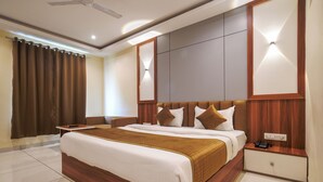 A hotel room with a large bed, a bedside table, a nightstand, and a ceiling fan. - Hotel Radhe Krishna Resort (Ujjain)