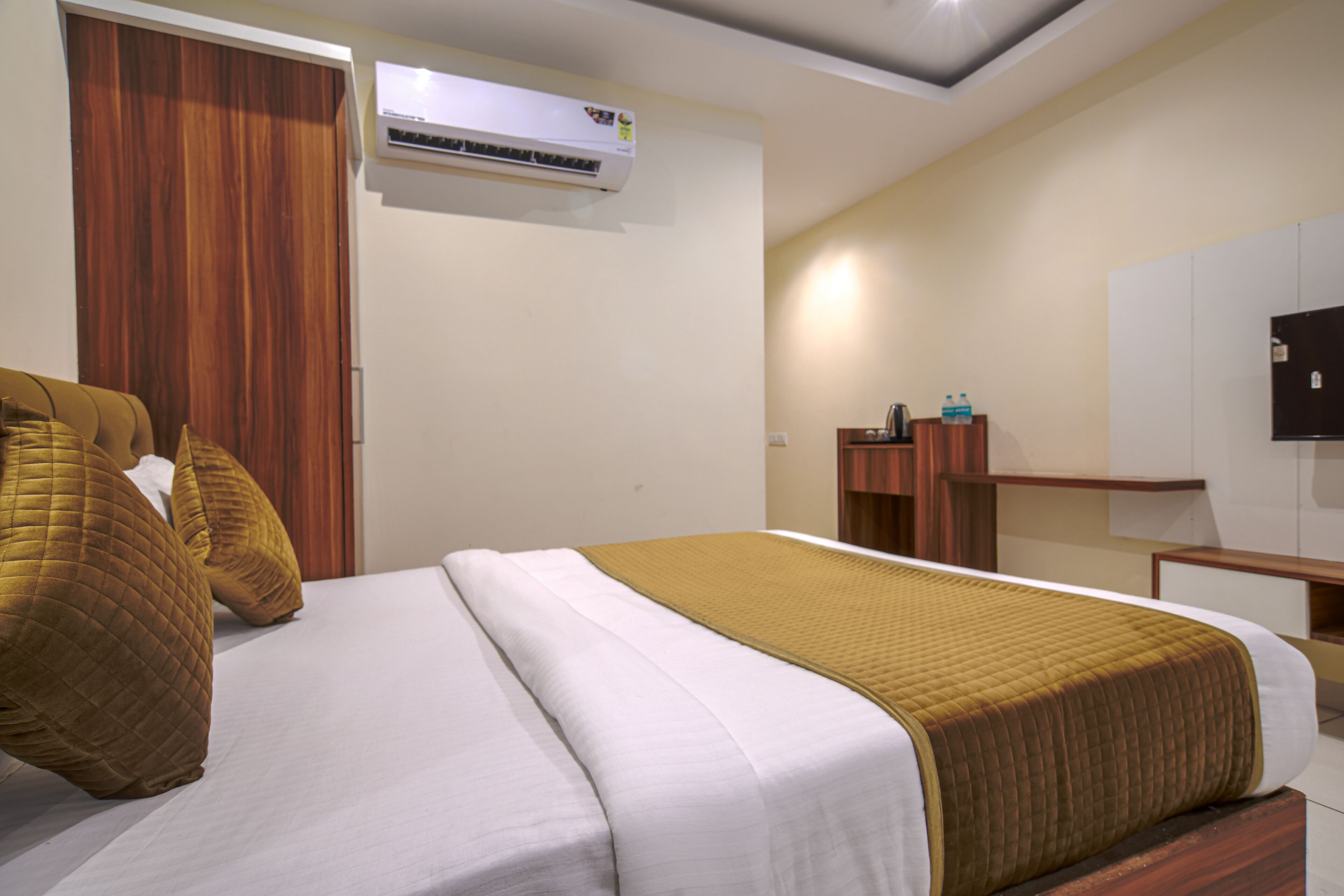 A hotel room with a bed, a wardrobe, an air conditioning unit, a desk, and a television.