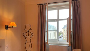 A hotel room with a large window, a radiator, a white chair, and a wall-mounted lamp. - 2 Bedroom Apartment in Saint-Malo (Saint-Malo)