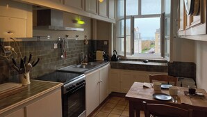 A modern kitchen with a large window, a dining area with a table set for two, and a view of the sea. - 2 Bedroom Apartment in Saint-Malo (Saint-Malo)