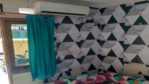 A room with a bed, teal curtains, patterned wallpaper, and an air conditioning unit. - OYO 93887 John Residence (Jakarta)