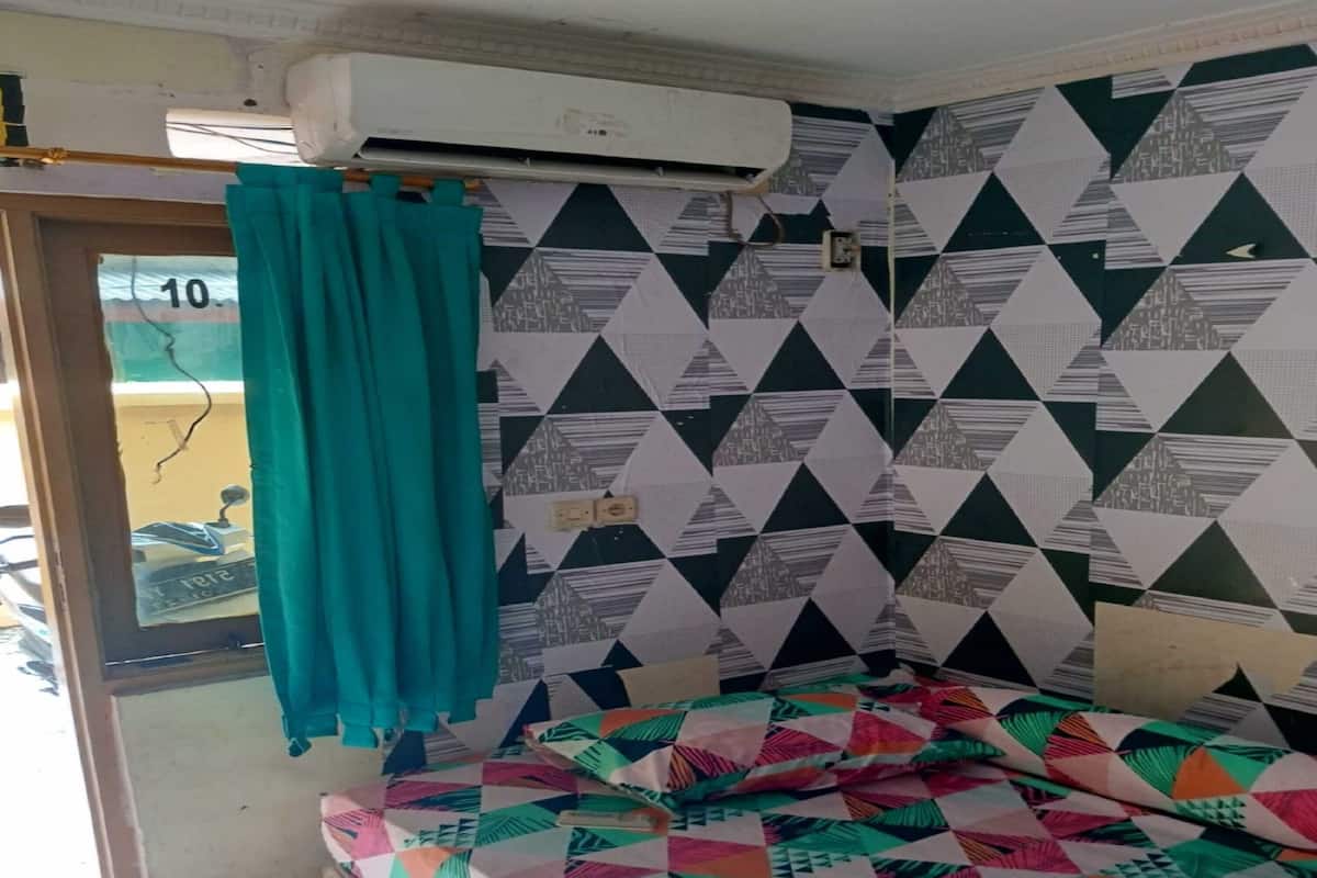 Ein Zimmer mit einem Bett, blaustichigem Vorhang, gemustertem Wandpapier und einer Klimaanlage.