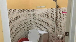 A small bathroom with a toilet, a shower, and a red bucket. - OYO 93887 John Residence (Jakarta)