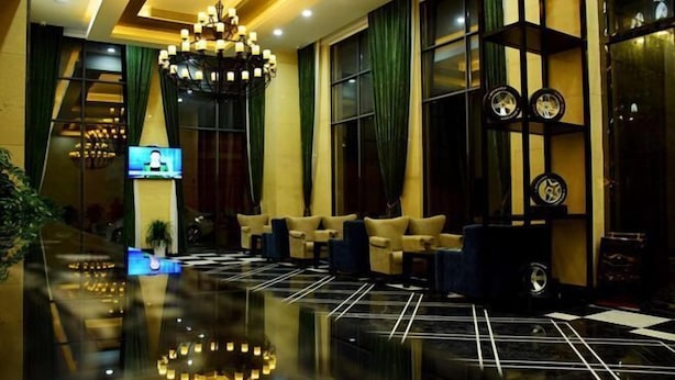 Un vestíbulo con piso reflectante, una araña de cristal, sofás y una pantalla de televisión.