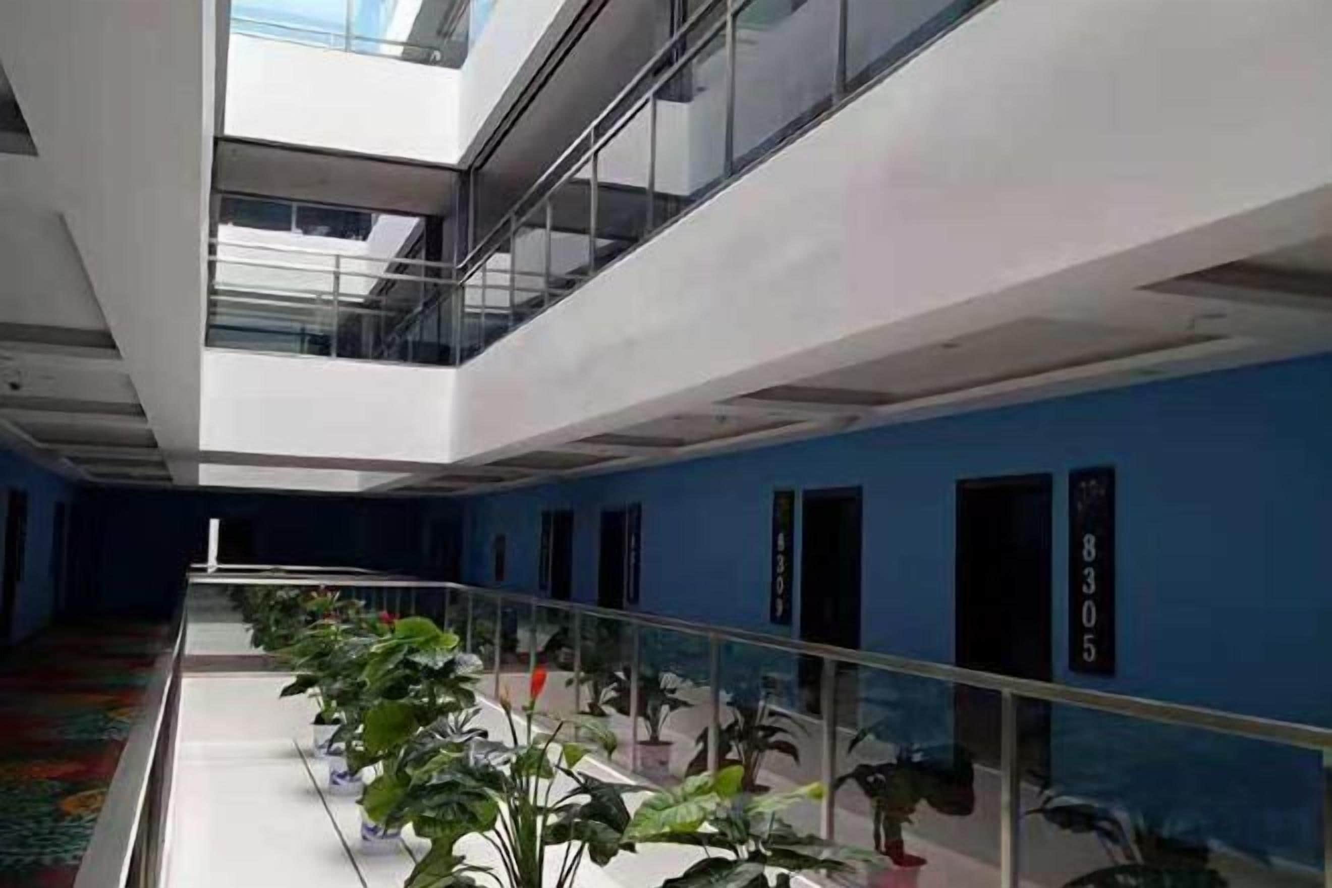 Un intérieur d’hôtel moderne avec une rambarde en verre, des plantes en pot et un mur d’accent bleu.