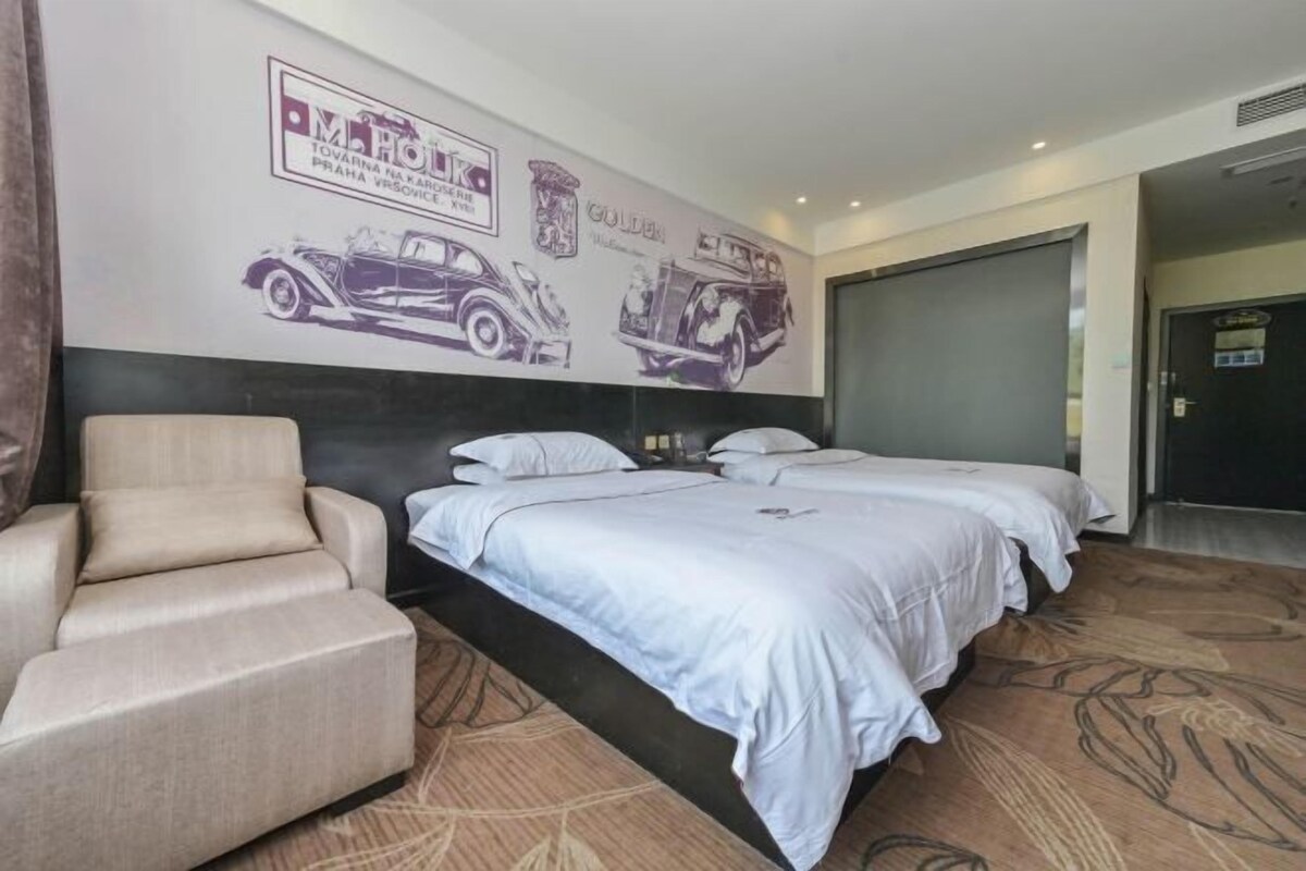 Habitación de hotel con cama, dos mesitas de noche, una silla e ilustraciones de coches en la pared.