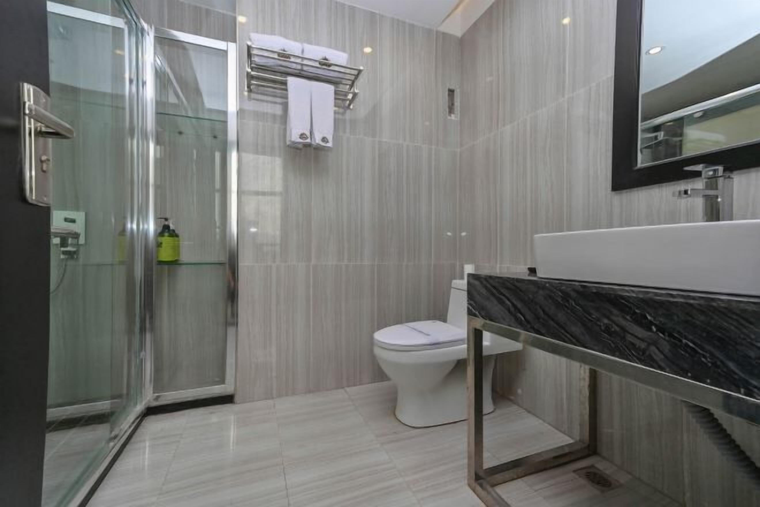A modern bathroom with a glass shower enclosure, a white toilet, and a black marble sink.