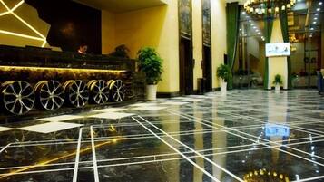 A lobby with a reception desk, potted plants, and a chandelier.