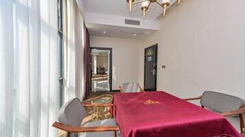A hotel room with a dining area featuring a table with a red tablecloth, two chairs, and a chandelier.
