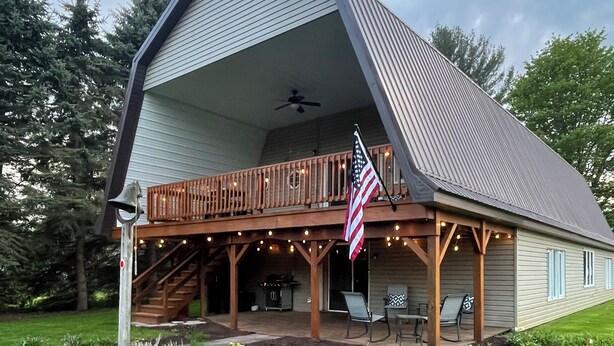 A large, single-story house with a sloped roof, a covered porch with string lights, and an American flag. - Big Barn in Bemus Point, unique, peaceful, and memorable (Bemus Point)