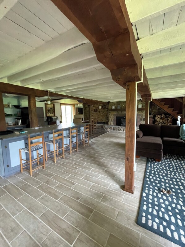 A spacious kitchen with a bar area, stone fireplace, and a patterned rug. - Big Barn in Bemus Point, unique, peaceful, and memorable (Bemus Point)