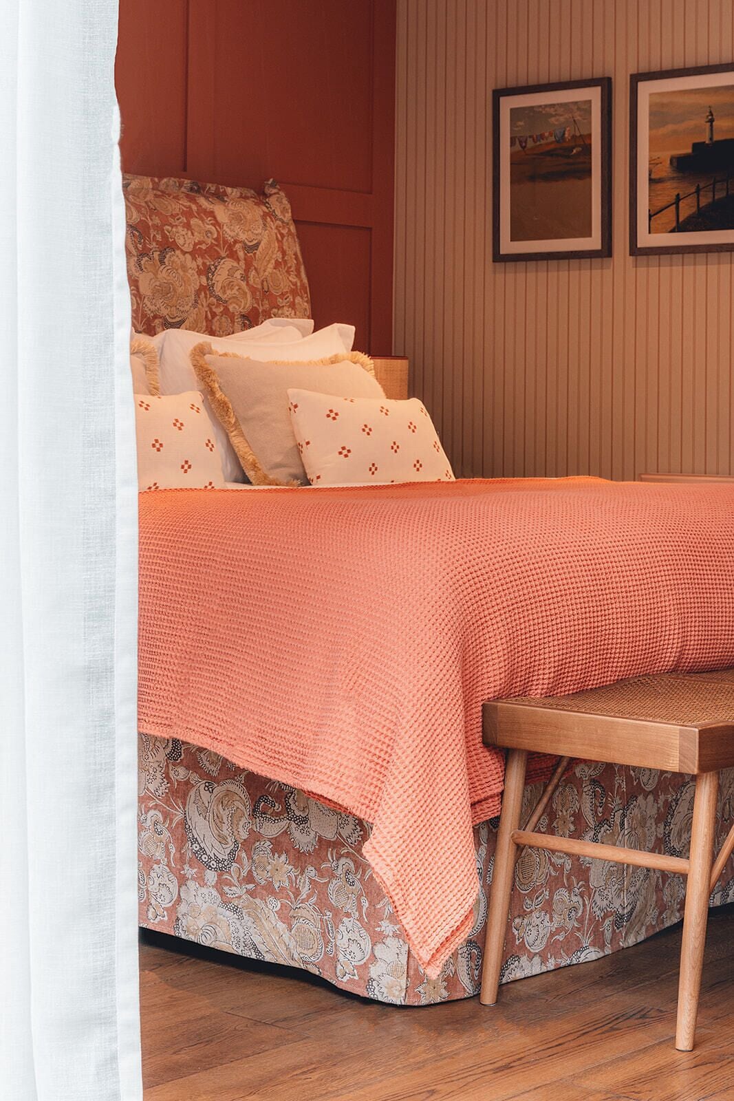 A neatly made bed with patterned bedding, a wooden bench, and two framed pictures on the wall.