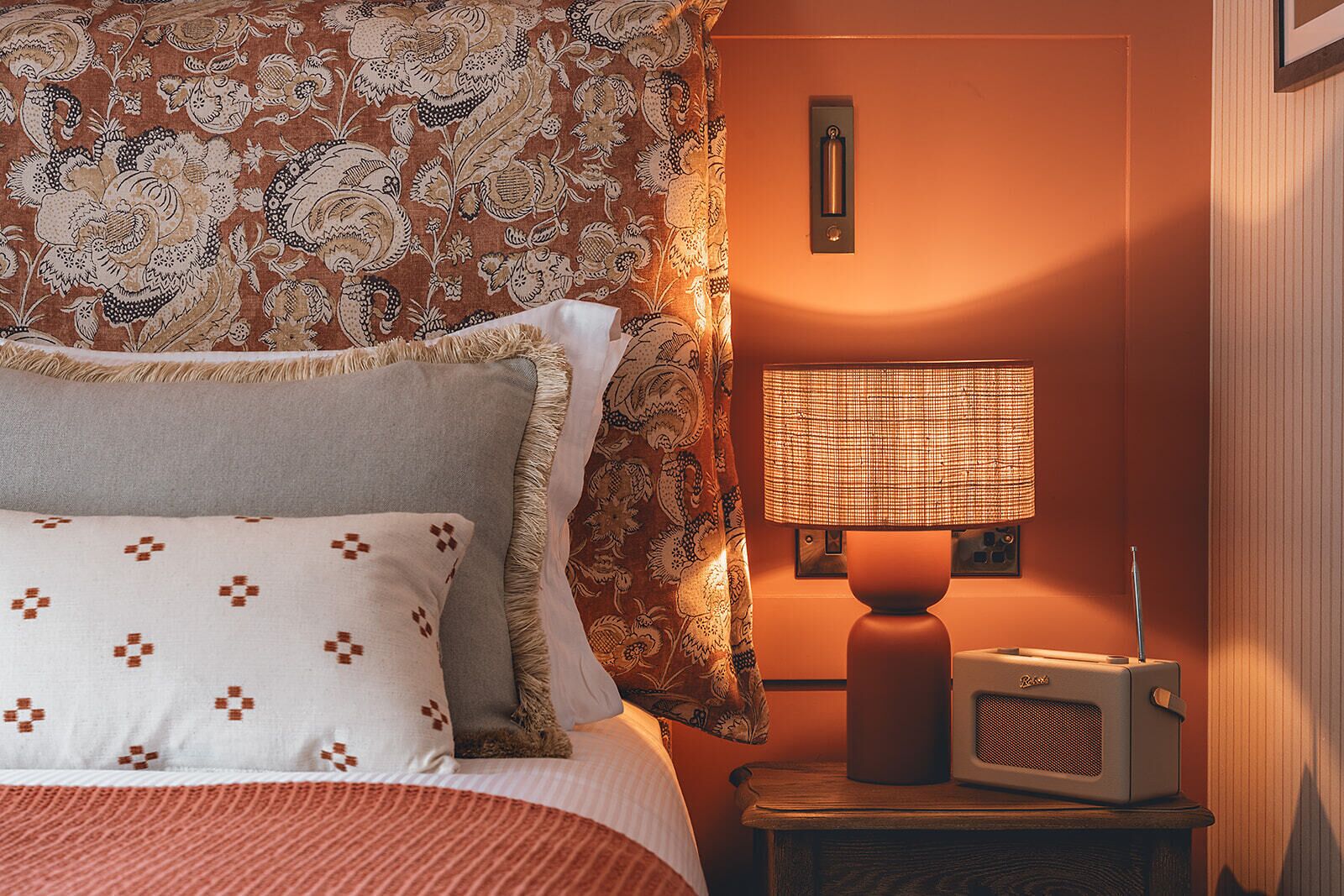 Una habitación de hotel con cama, cortinas estampadas, una lámpara de noche y una radio.