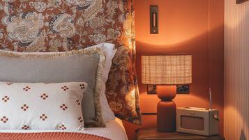 Una habitación de hotel con cama, cortinas estampadas, una lámpara de noche y una radio.