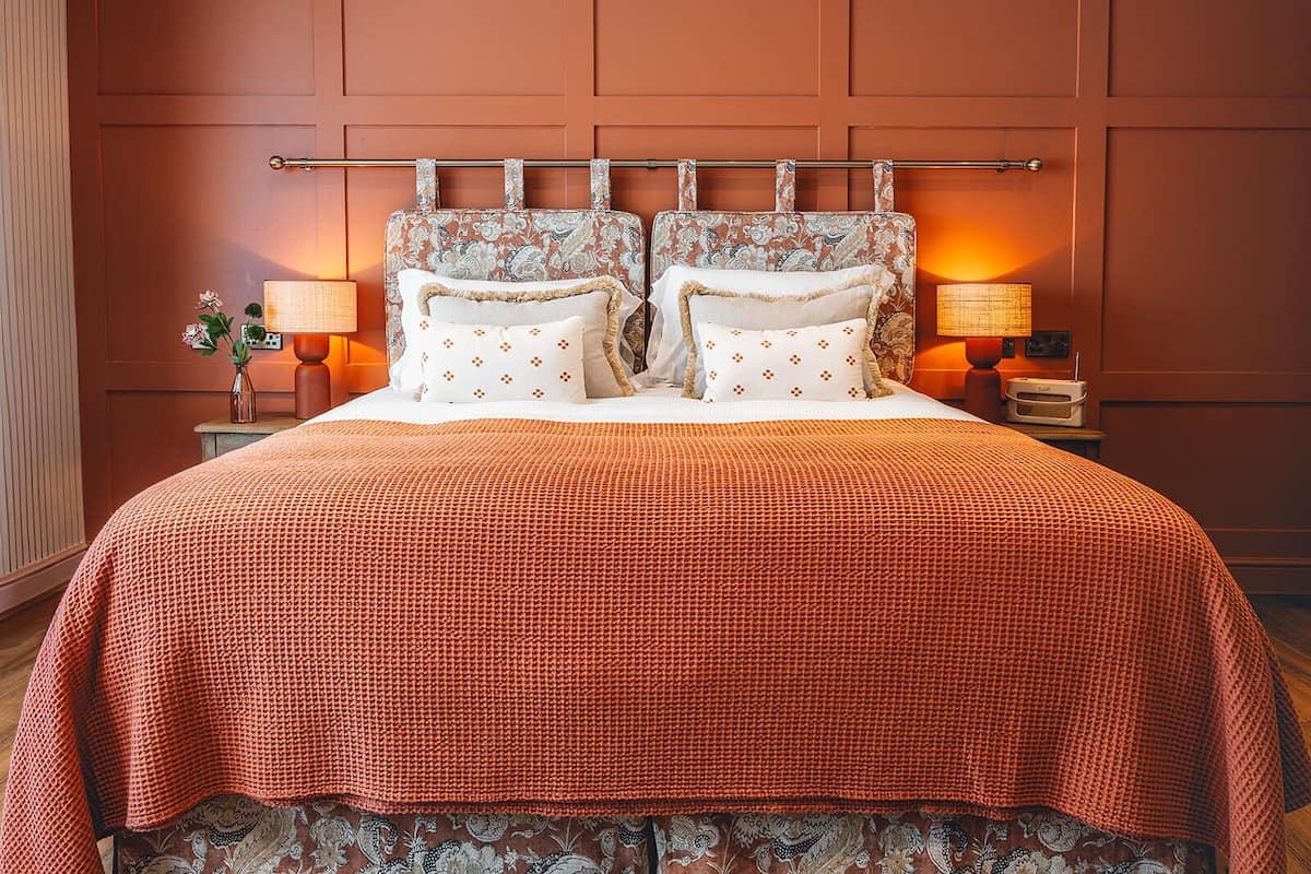 Una cama con un cabecero estampado, dos lámparas de noche y un jarrón decorativo sobre la mesita.