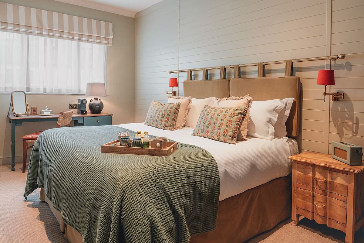Un dormitorio ordenado con cama, mesitas de noche, escritorio y ventana con cortinas.