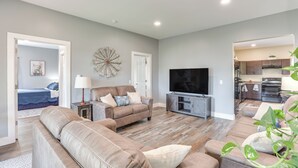 A modern living room with a large sofa, a TV, and a dining area visible through an open door. - Wisconsin Farmhouse Stay: Utv, Boat, Snowmobile! (Monroe)