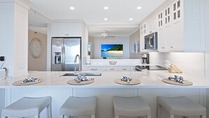 A modern kitchen with white cabinetry, a central island with bar stools, a stainless steel refrigerator, and a ceiling fan. - Panoramic Gulf Views, Newly Renovated, Spectacular Sunsets in Naples (Naples)
