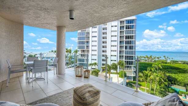 A balcony with a view of a modern building, a dining area with chairs and a table, and a woven pouf. - Panoramic Gulf Views, Newly Renovated, Spectacular Sunsets in Naples (Naples)