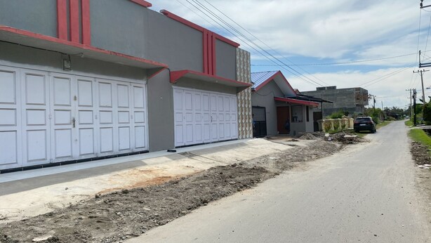 Una calle residencial con dos garajes, una casa con techo rojo y un automóvil estacionado.