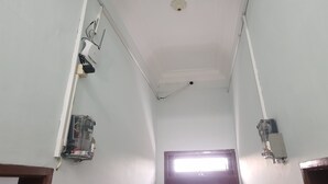 Un pasillo estrecho con una ventana al final, paredes blancas y cajas eléctricas en el techo.
