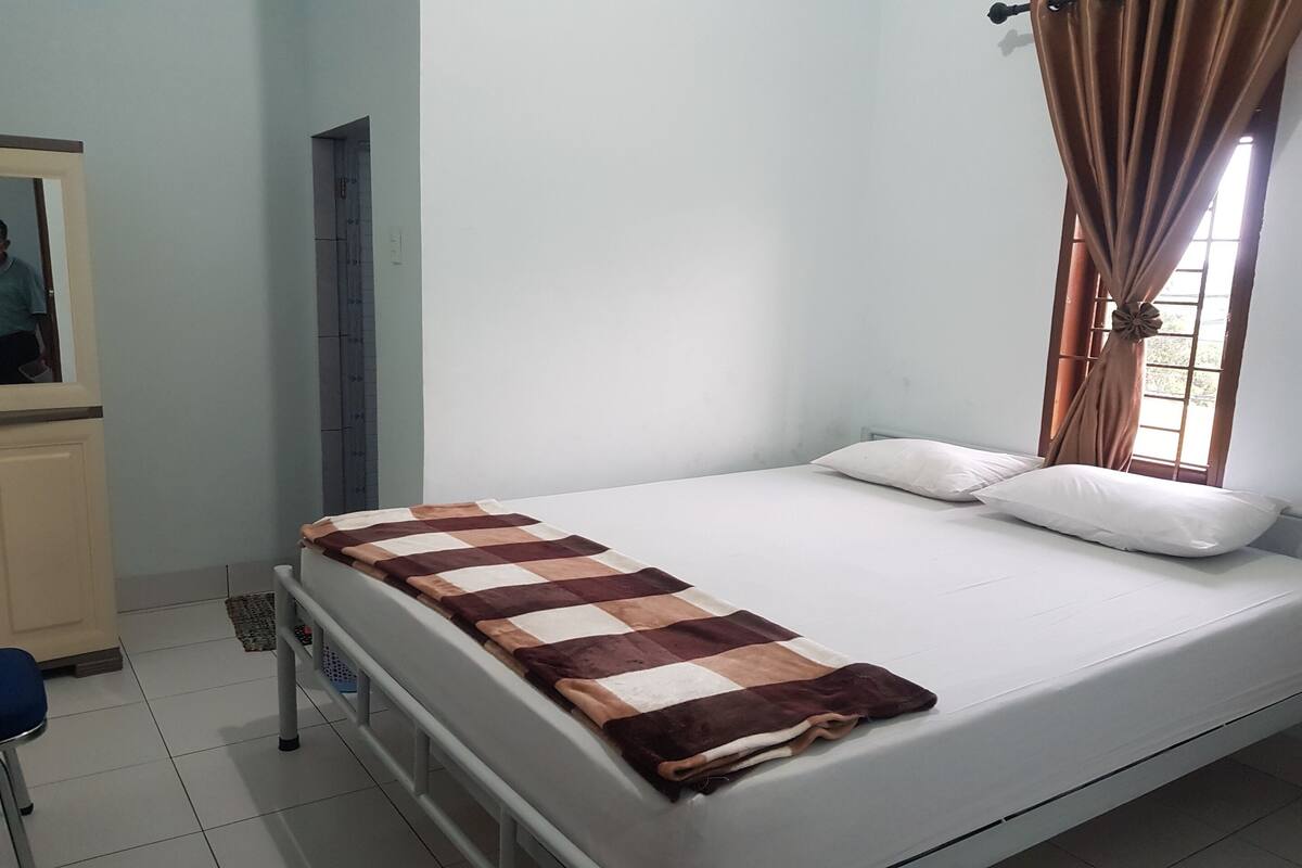 A single bed with a checkered blanket, white pillows, and a window with curtains.