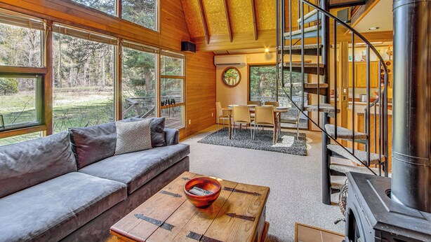 A modern interior with a wooden ceiling, a staircase, a cozy seating area, and a large window offering a view of the outdoors. - Cle Elum A-frame - Direct Yakima River Access! (Cle Elum)