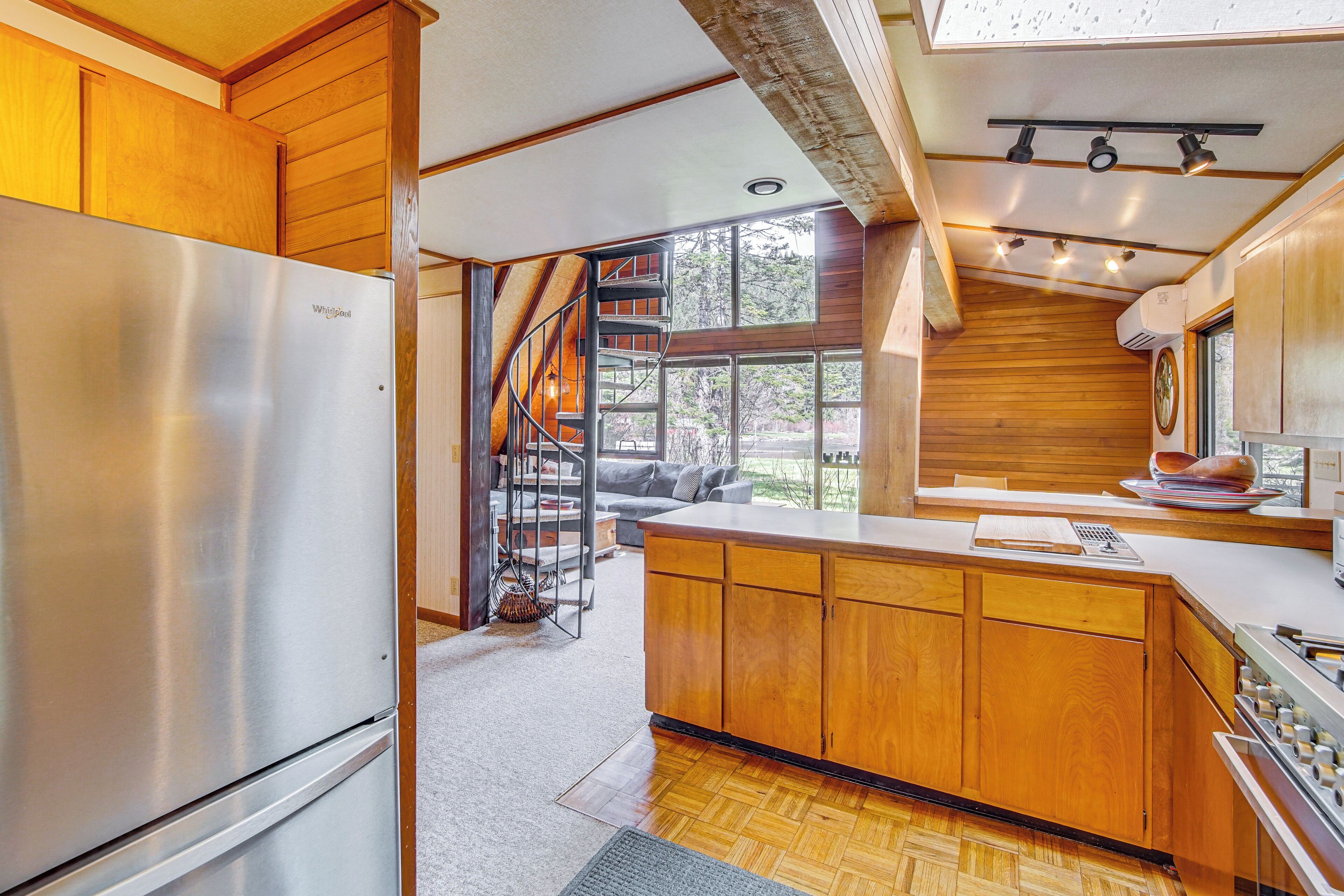 A modern kitchen with wooden cabinets, a stainless steel refrigerator, a built-in stove, and a large window offering a view of the outdoors.