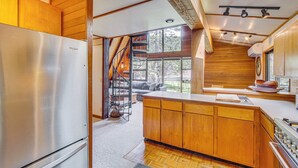 A modern kitchen with wooden cabinets, a stainless steel refrigerator, a built-in stove, and a large window offering a view of the outdoors. - Cle Elum A-frame - Direct Yakima River Access! (Cle Elum)